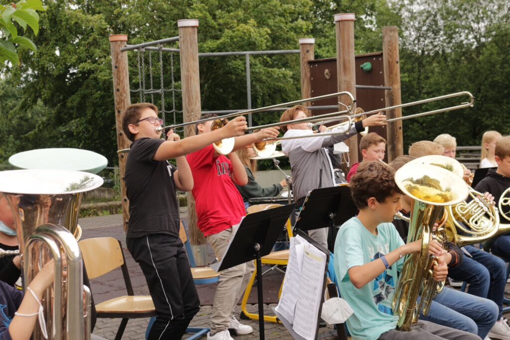 Musikschüler spielen verschiedene Blasinstrumente im Freien.