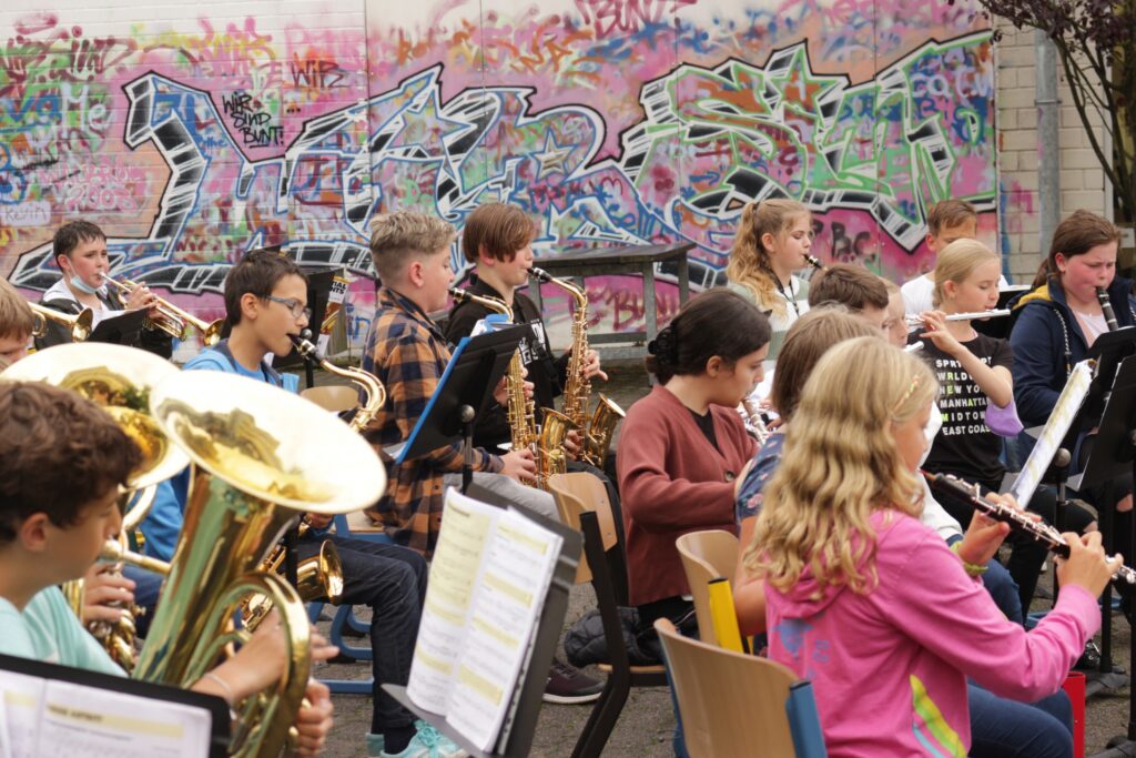 Schüler spielen in einem Schulorchester vor einer bunten Graffiti-Wand.