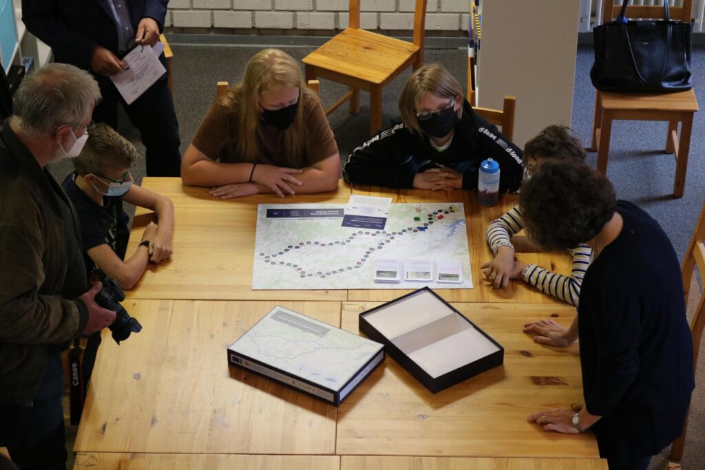 Gruppe von Personen schaut auf einen Plan auf einem Tisch in einem Klassenraum.