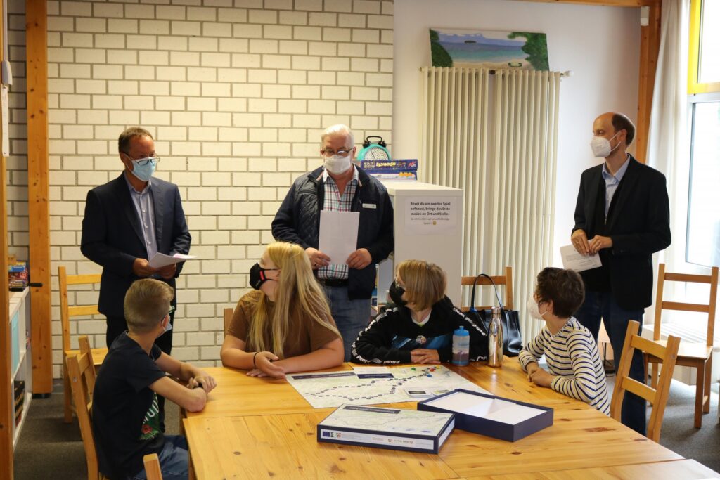 Gruppen von Personen stehen um einen Tisch, einige tragen Masken.