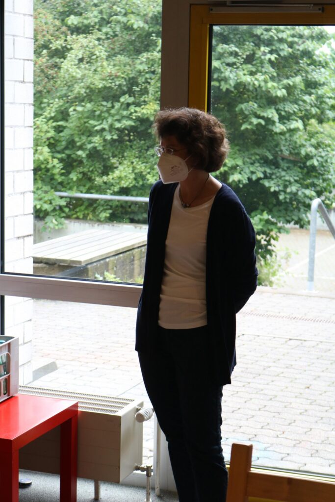 Frau steht in einem Raum neben einem Fenster mit Blick ins Grüne.