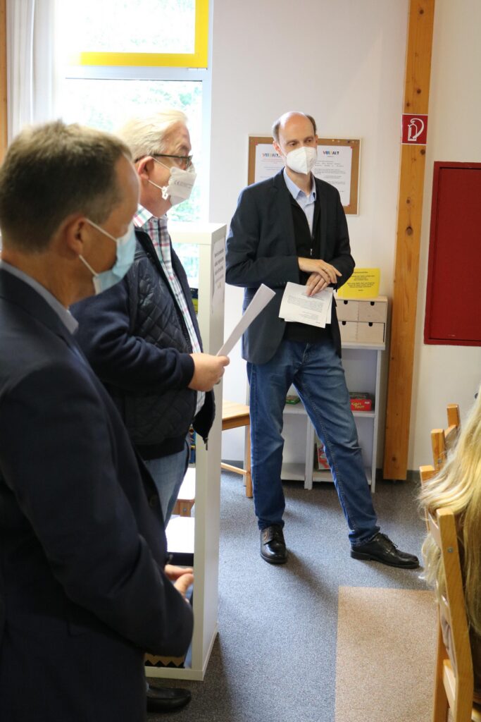 Personen in einem Klassenzimmer während einer Besprechung, alle tragen Masken.