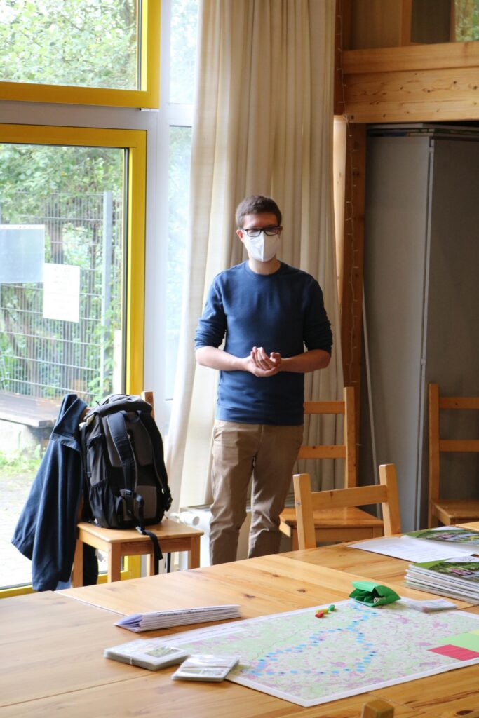 Mann mit Maske steht in einem Raum neben einem Tisch.