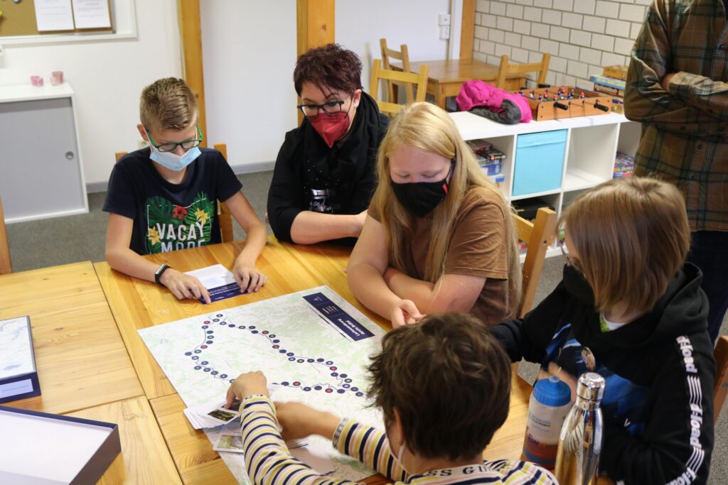 Gruppentreffen am Tisch mit Karten und Notizen. Teilnehmer tragen Masken.
