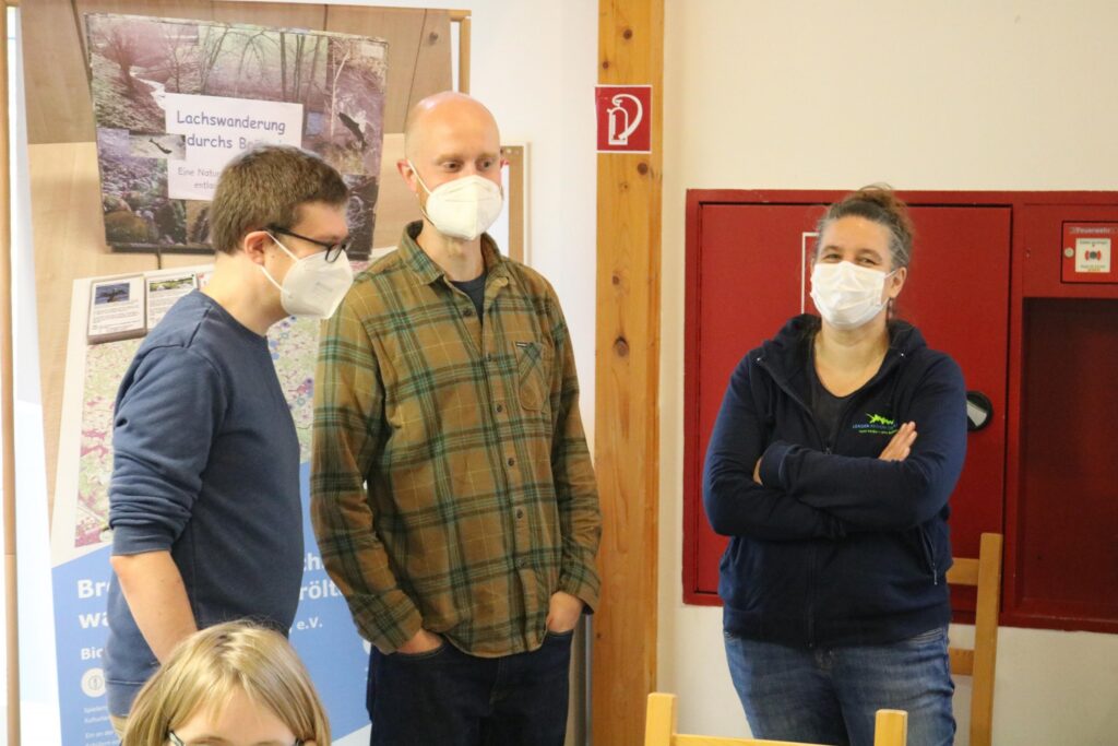Drei Personen im Gespräch, alle tragen Schutzmasken.