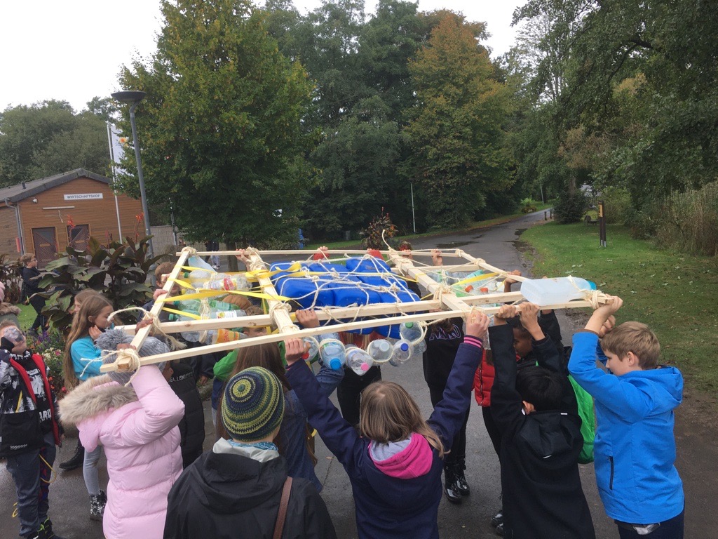 Kinder tragen gemeinsam eine Konstruktion aus Holz und Flaschen.