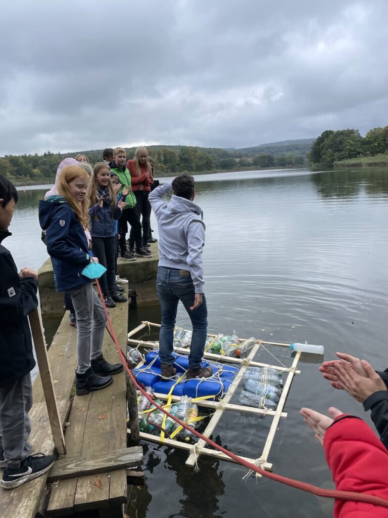 Gruppen von Schülern stehen an einem Steg und beobachten eine Flotte aus Bottichen.