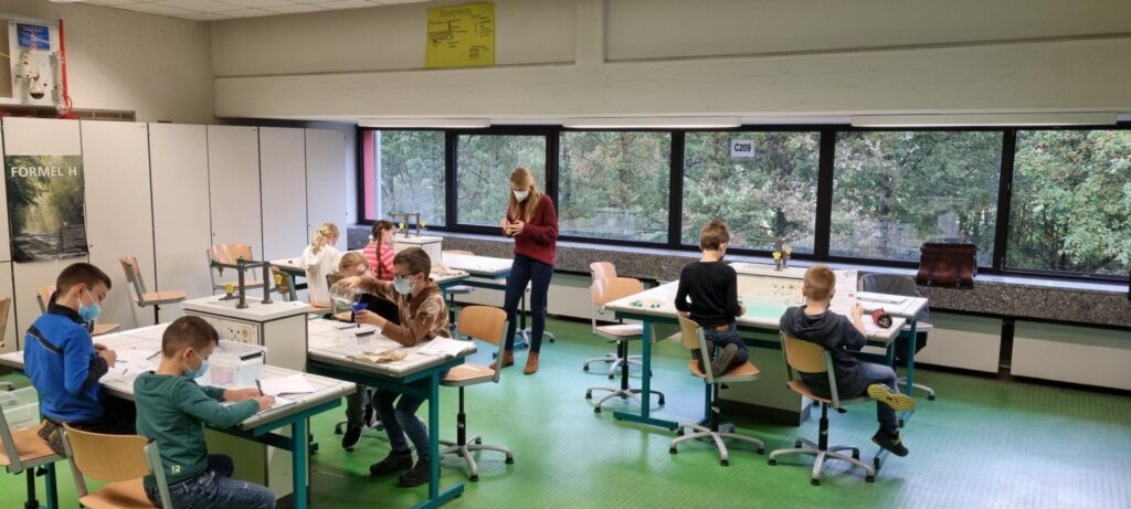 Schüler arbeiten an Tischen in einem Klassenraum mit Fenstern.