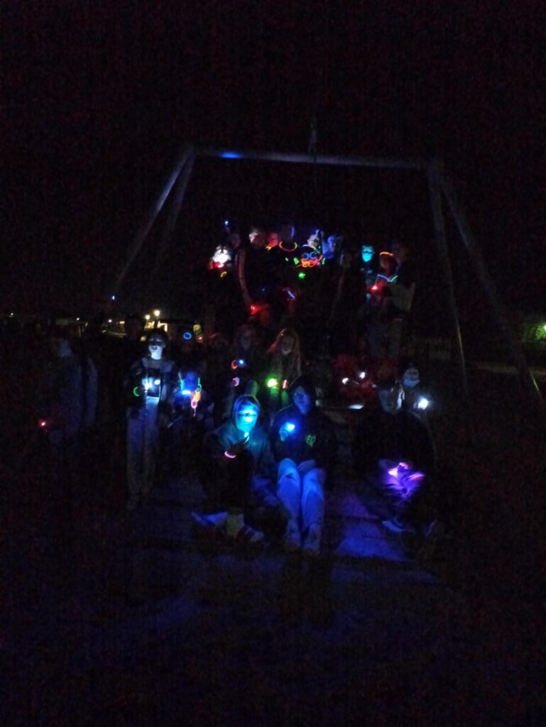 Gruppe von Personen mit leuchtenden Accessoires auf einem Spielplatz bei Nacht.