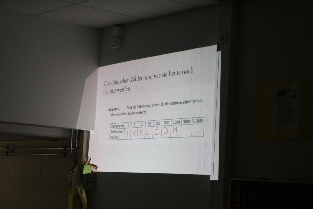 Ein Projektor zeigt einen Text mit Informationen und einer Tabelle an einer Wand.
