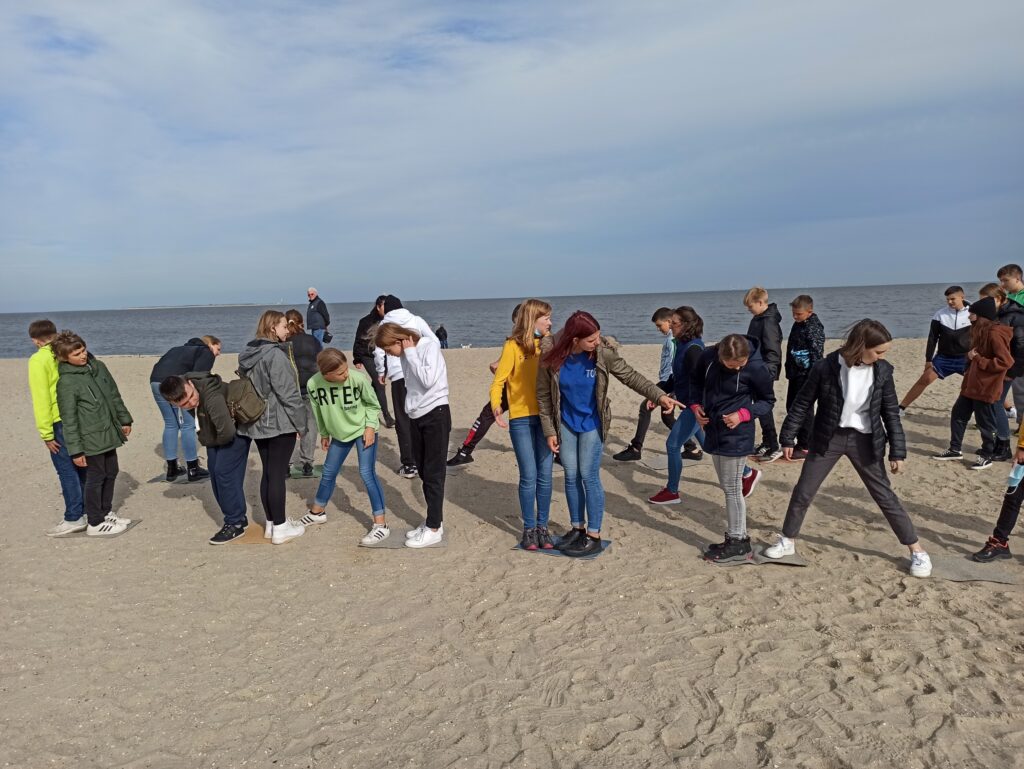 Schüler stehen paarweise am Strand und üben eine Teamaktivität.