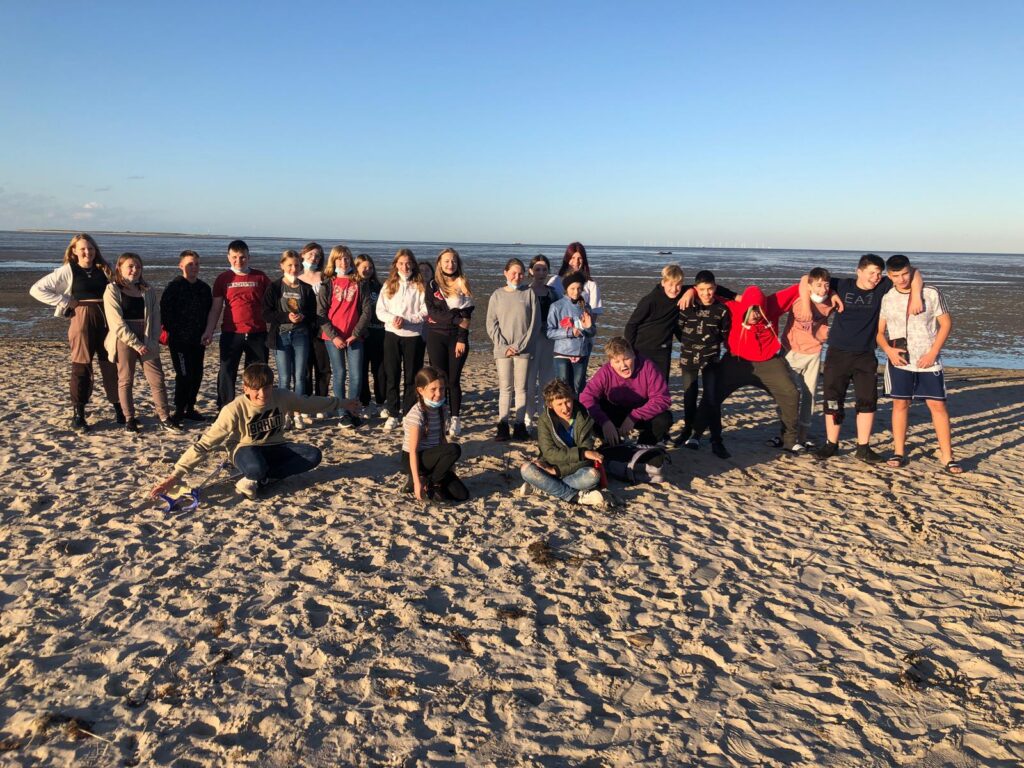 Gruppe von Schülerinnen und Schülern am Strand bei Sonnenlicht.