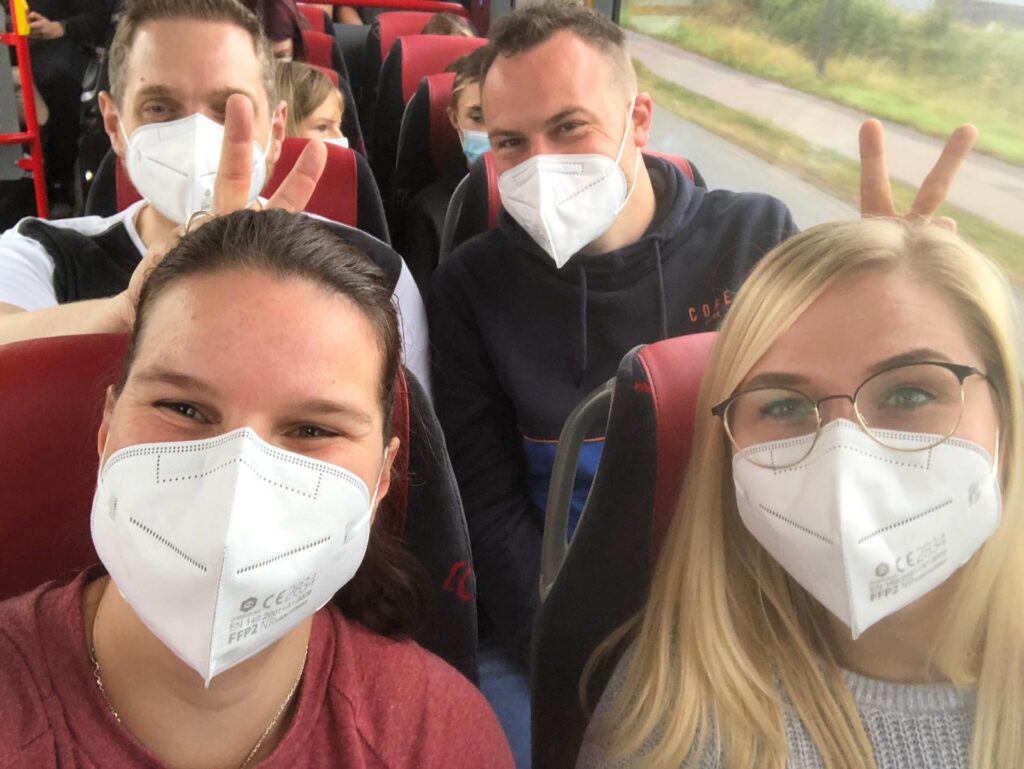 Gruppenselfie von Personen in einem Bus mit Atemschutzmasken.