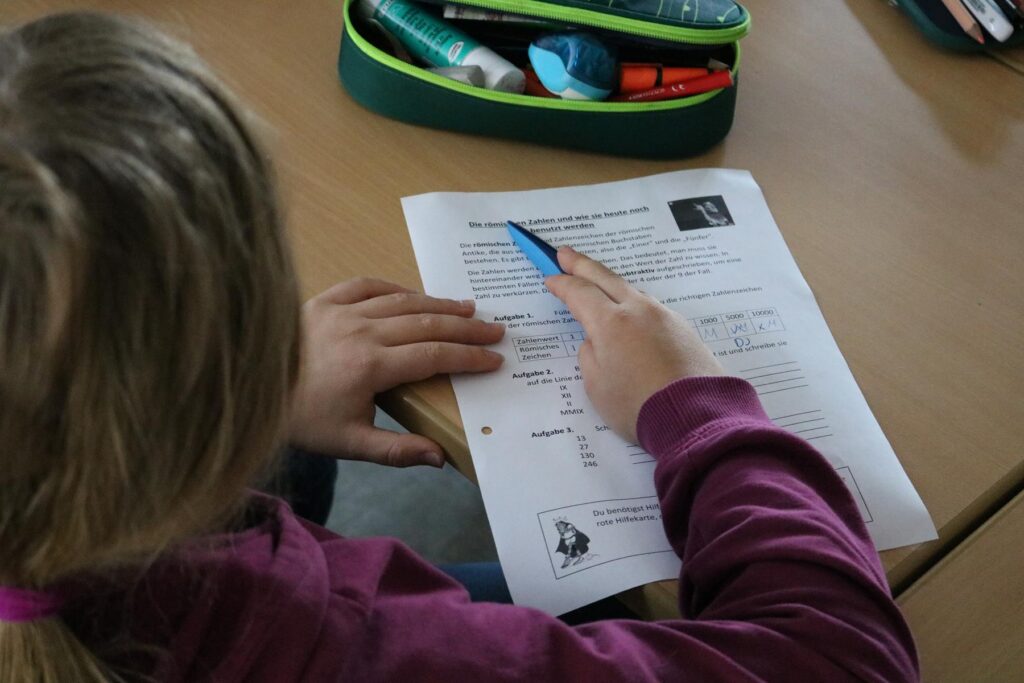 Eine Hand hält einen Stift und zeigt auf ein Arbeitsblatt.