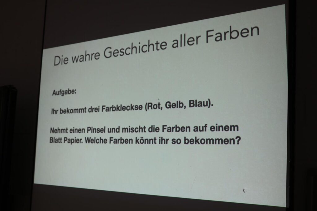 Tafel mit der Aufgabe zur Farbmischung: Rot, Gelb, Blau auf Papier.