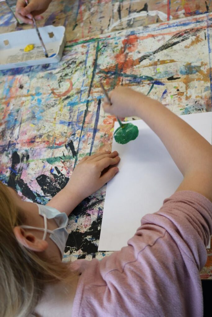 Ein Schüler malt mit grünem Material auf einem Blatt Papier.