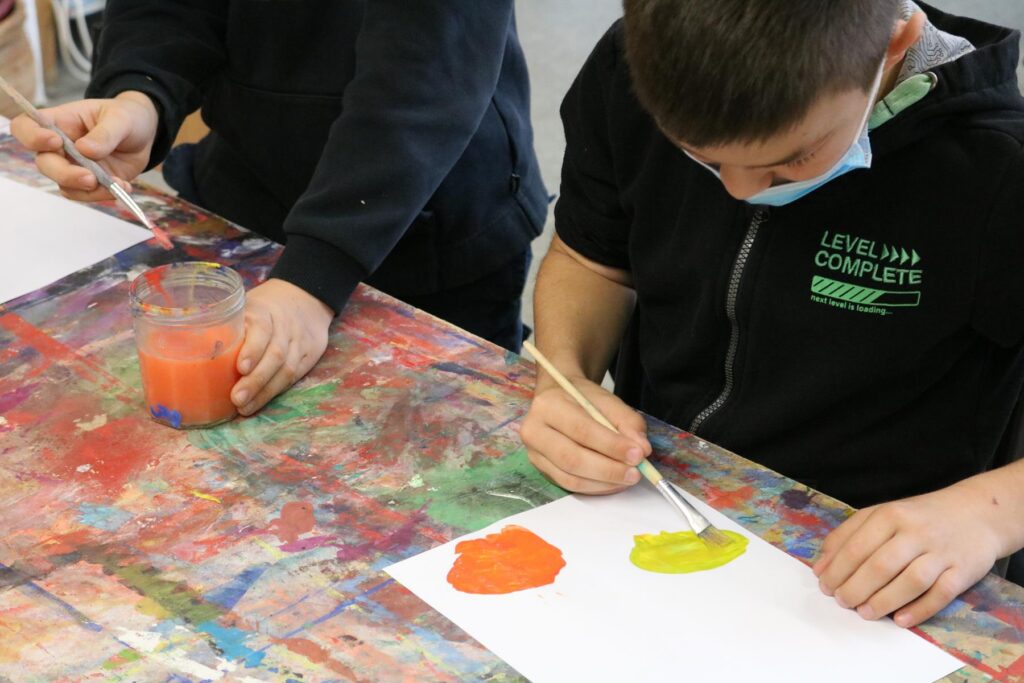 Schüler malen mit Pinsel und Wasserfarben auf Papier.