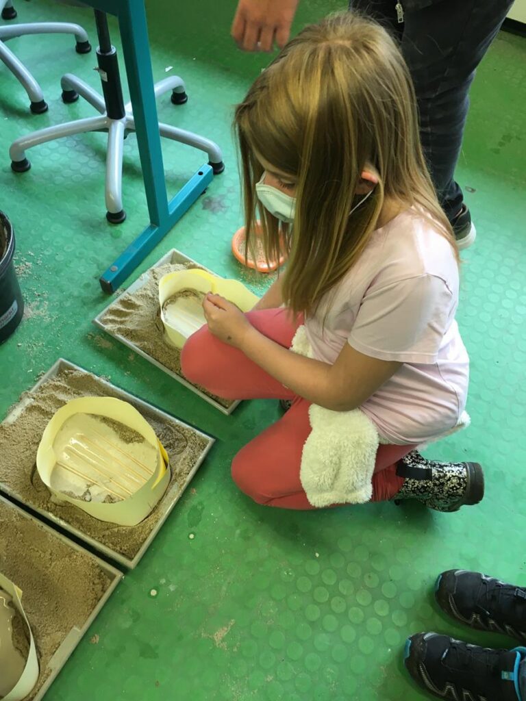 Ein Mädchen kniet auf dem Boden und arbeitet mit Sand in einem Klassenzimmer.