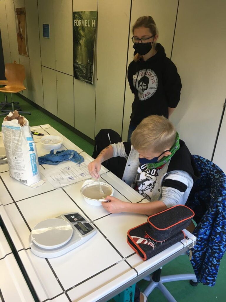 Kind mixt etwas in einer Schüssel, ein weiteres Kind beobachtet.