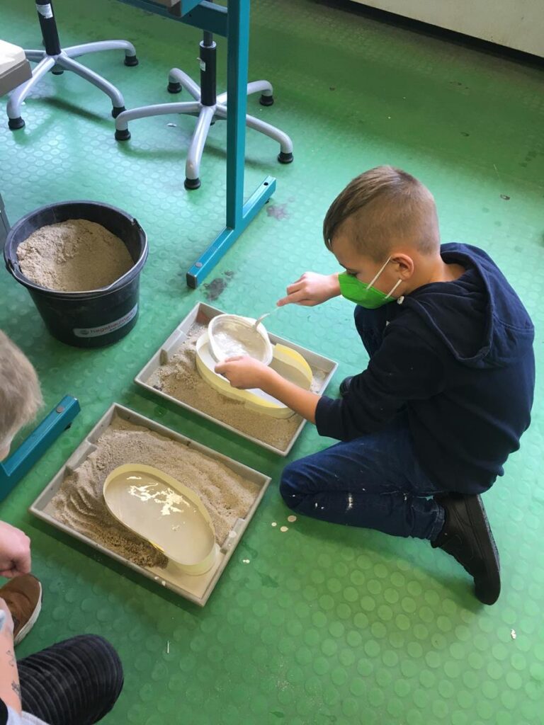 Schüler arbeitet mit Sand in Formkästen und modelliert Objekte.