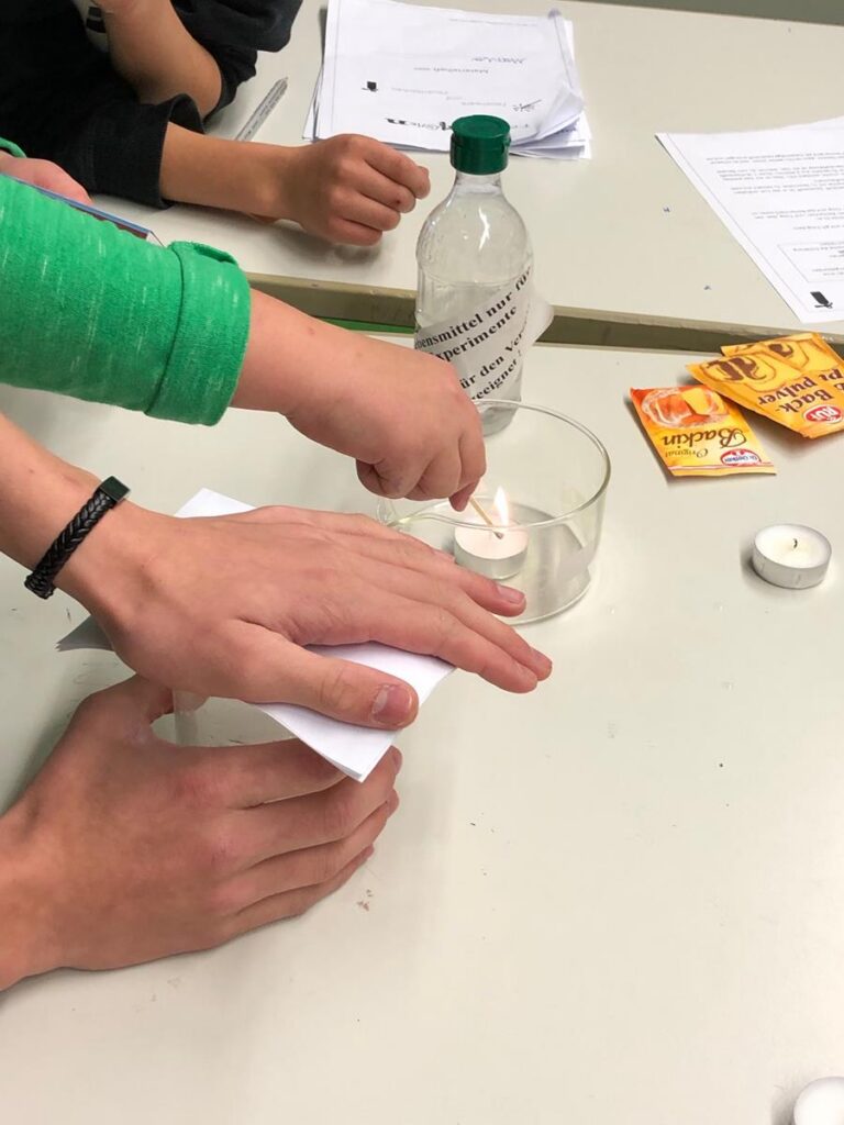 Schüler führen ein Experiment mit Kerze und Wasser durch.