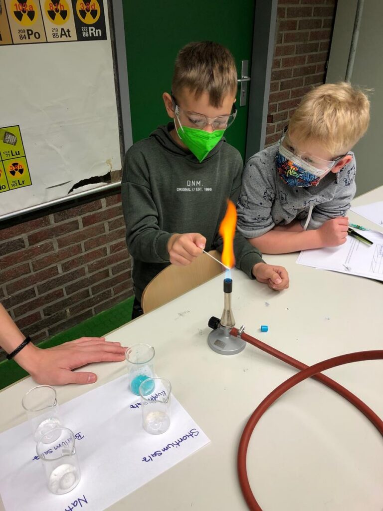 Schüler führen ein Experiment mit einer Flamme durch. Sicherheitsmaßnahmen sind sichtbar.