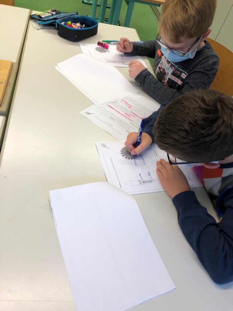 Zwei Kinder schreiben an einem Tisch, umgeben von Papier und Stiften.