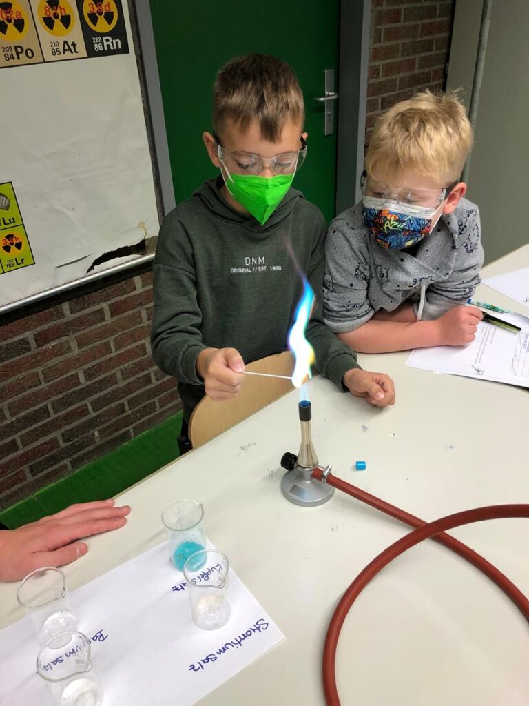 Zwei Kinder führen ein Experiment mit einer Flamme und verschiedenen Substanzen durch.