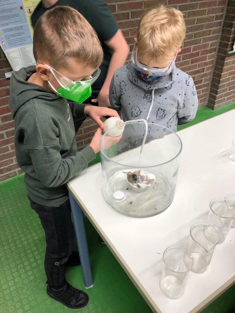 Junge Schüler führen ein Experiment mit einer Glasbehälter durch.