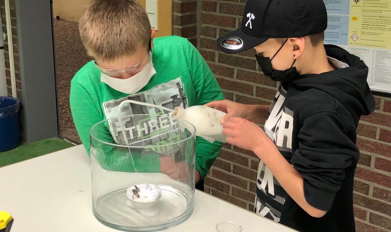 Zwei Schüler arbeiten gemeinsam an einem Experiment mit einem Behälter.