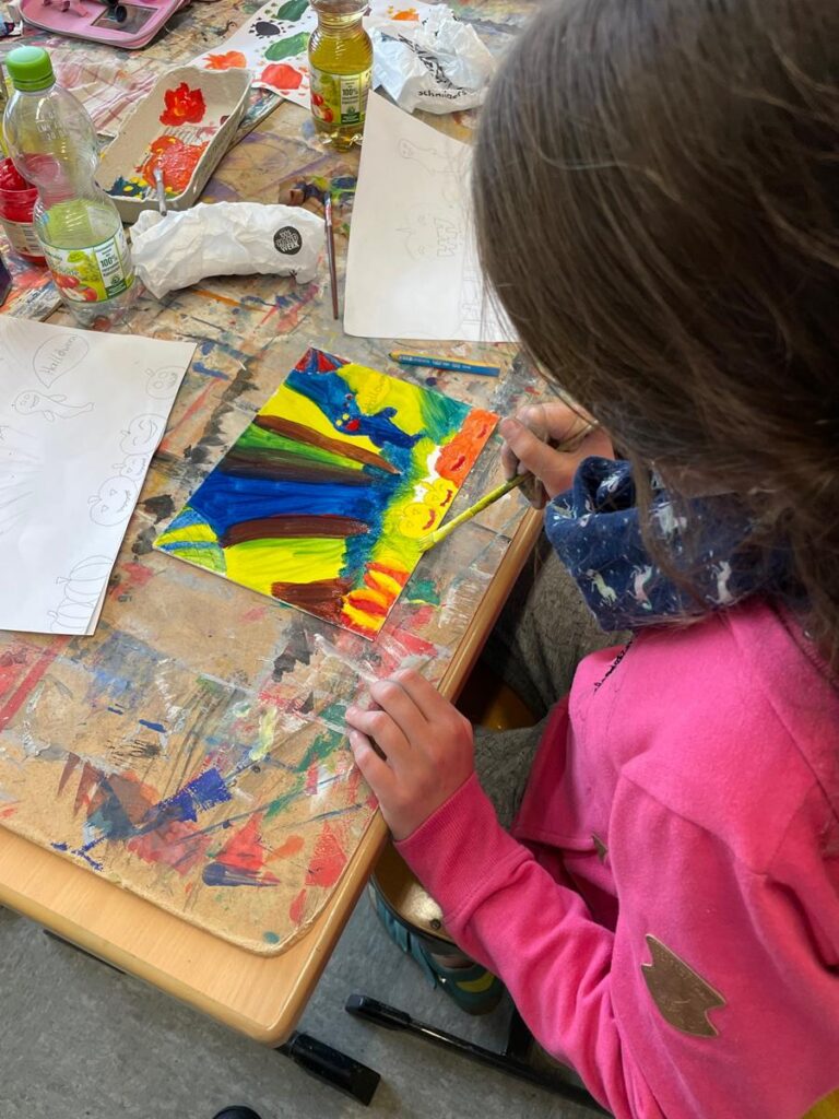 Ein Kind malt mit bunten Farben auf einem Blatt Papier.