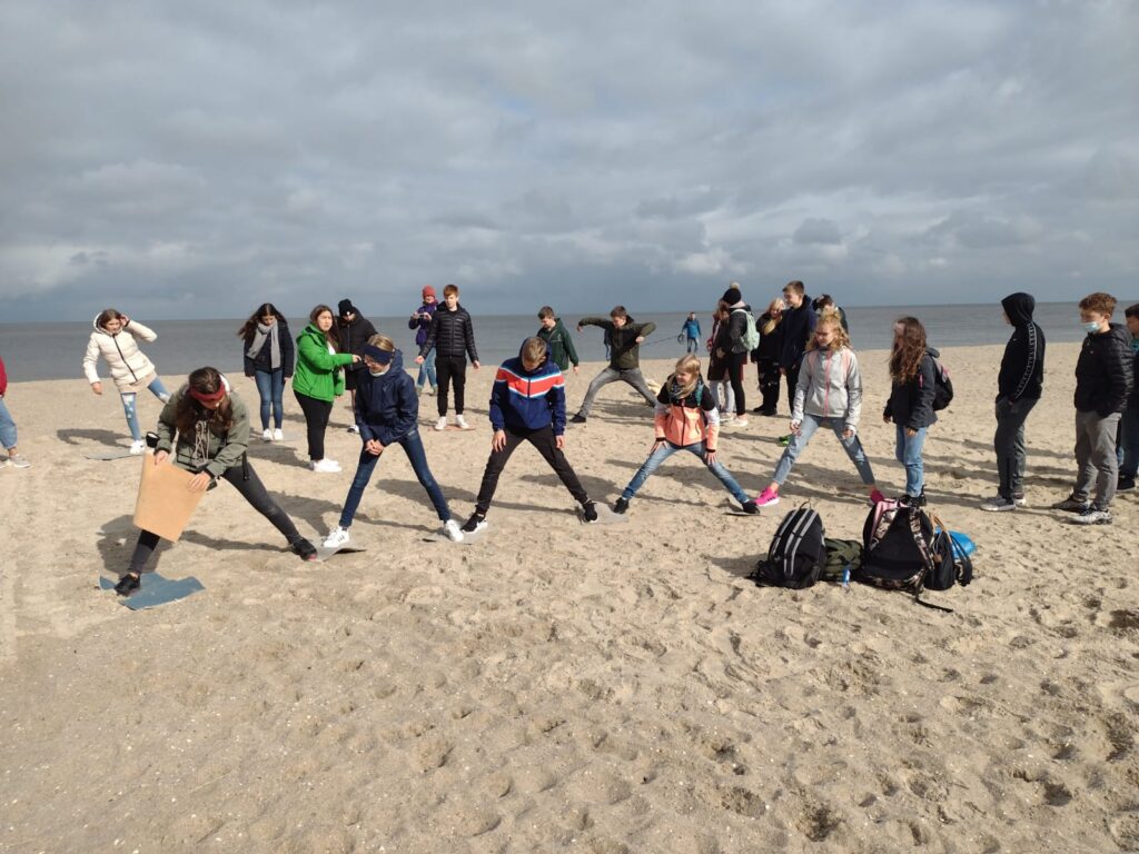 Schüler stehen am Strand und machen Dehnübungen in Gruppen. Wolkiger Himmel.