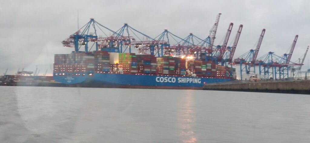 Großes Containerschiff im Hafen mit Kranen im Hintergrund.