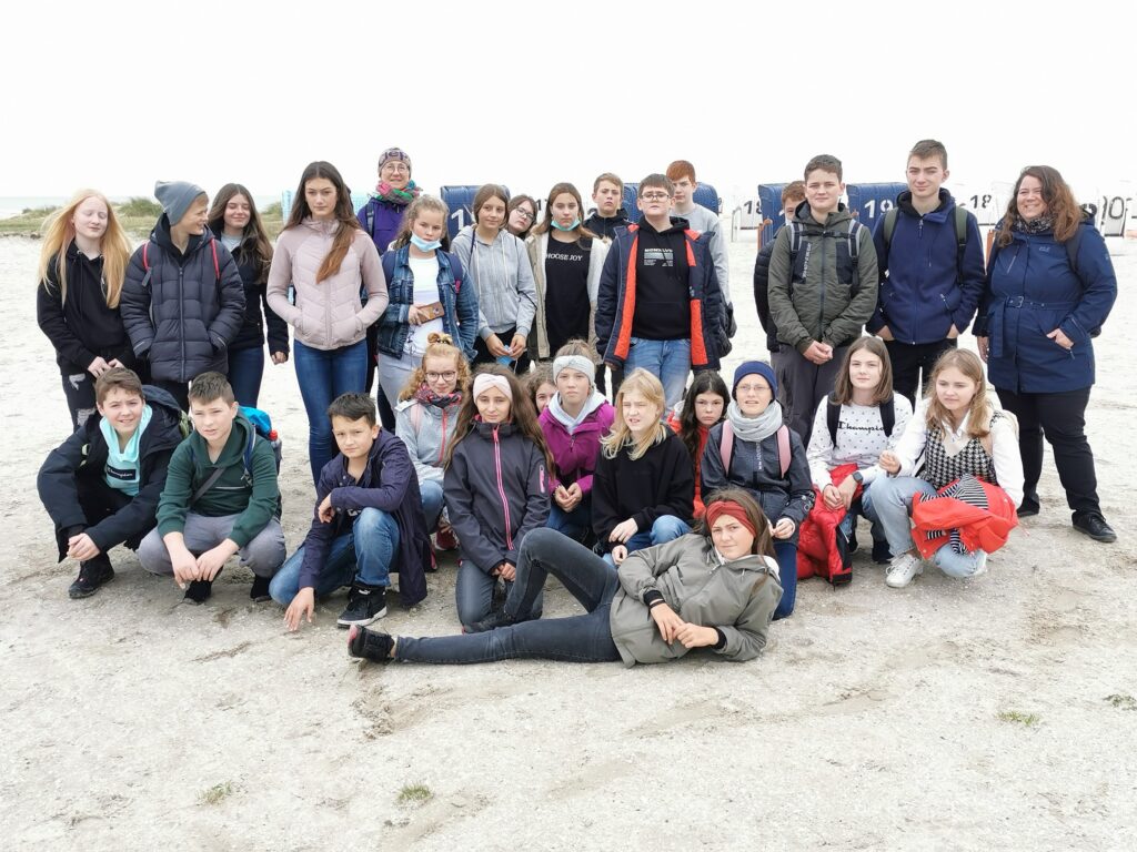 Gruppe von Schülern steht und sitzt auf sandigem Boden, mit mehreren behind.