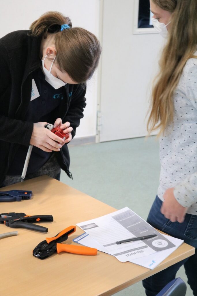 Zwei Schülerinnen arbeiten an einem Tisch mit Werkzeug und Unterlagen.