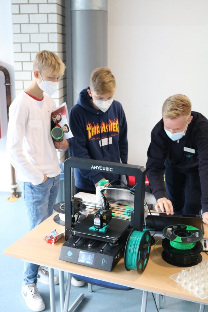 Schüler arbeiten an einem 3D-Drucker und besprechen deren Funktion.