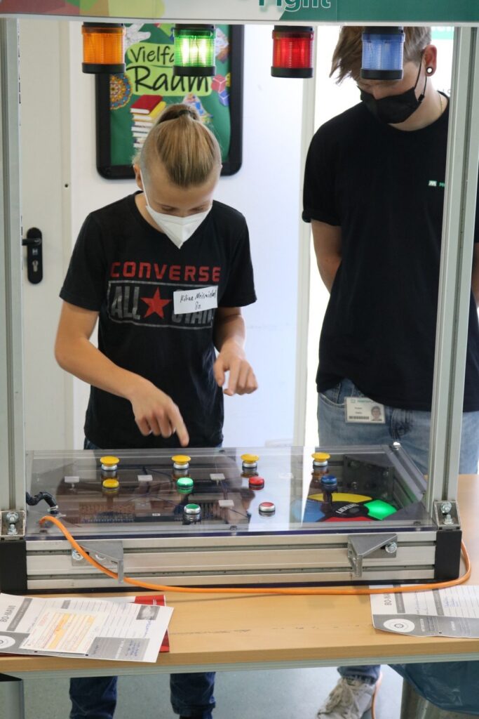 Schülerinnen und Schüler bedienen ein Experimentierfeld mit verschiedenen Knöpfen.
