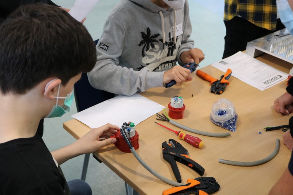Schüler arbeiten an Kabelverbindungen mit Werkzeugen und Materialien auf einem Tisch.