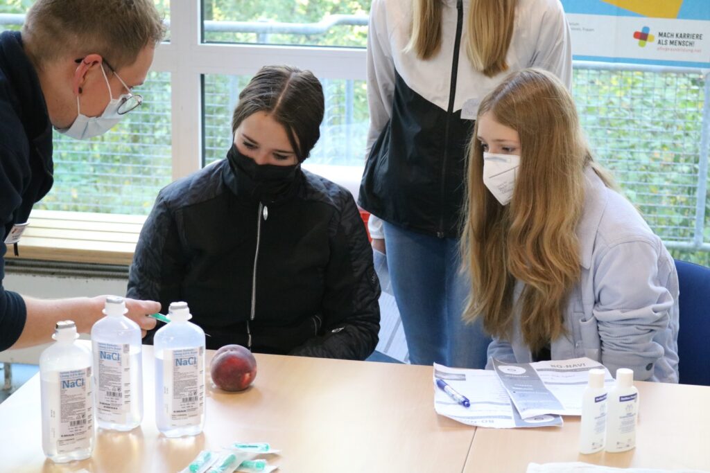 Schülerinnen beobachten eine Demonstration mit Flaschen und einem Apfel.
