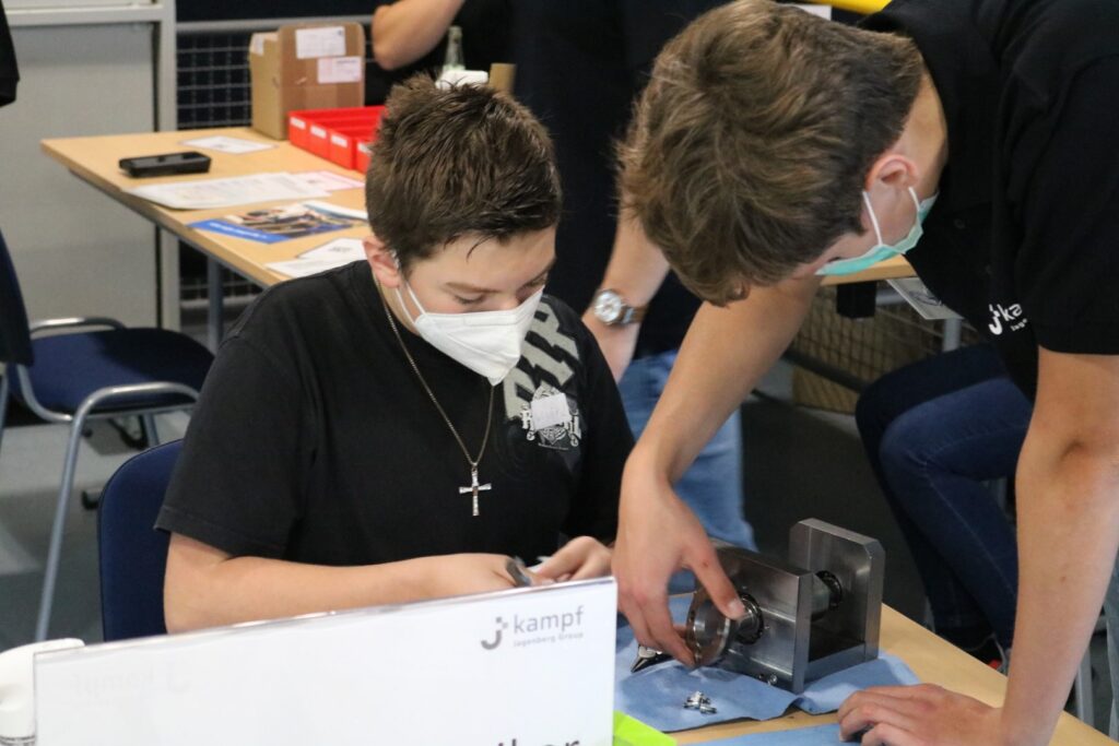 Schüler arbeitet an einem Projekt, unterstützt von einem Helfer. Beide tragen Masken.
