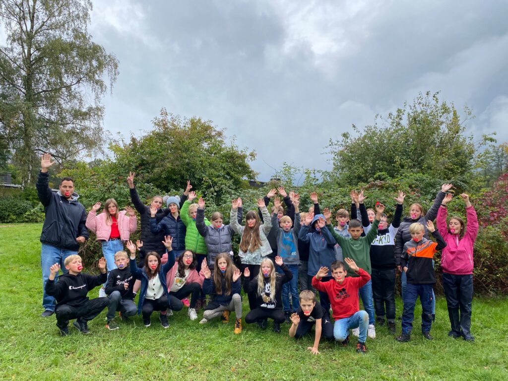 Gruppenfoto von Schülern mit erhobenen Händen im Freien. Gewitterhafte Wolken im Hintergrund.