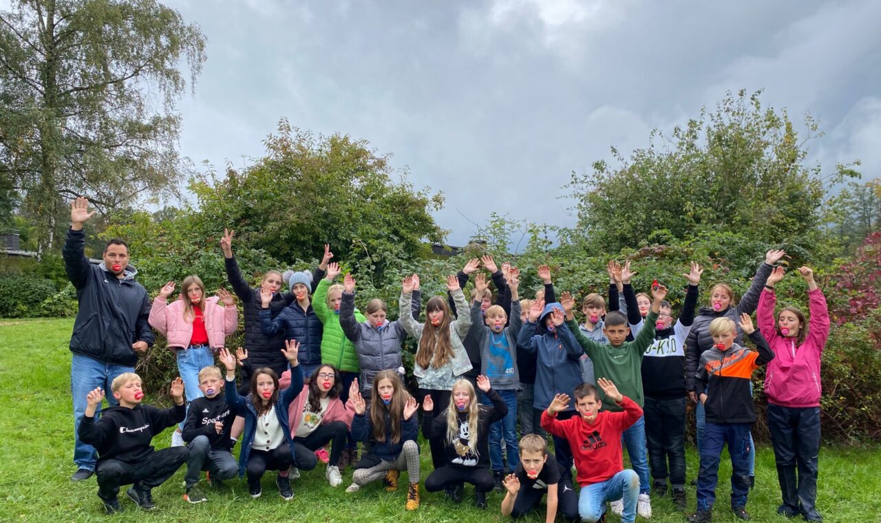Gruppenfoto von Schülern mit erhobenen Händen im Freien. Gewitterhafte Wolken im Hintergrund.