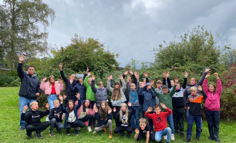Gruppenfoto von Schülern mit erhobenen Händen im Freien. Gewitterhafte Wolken im Hintergrund.