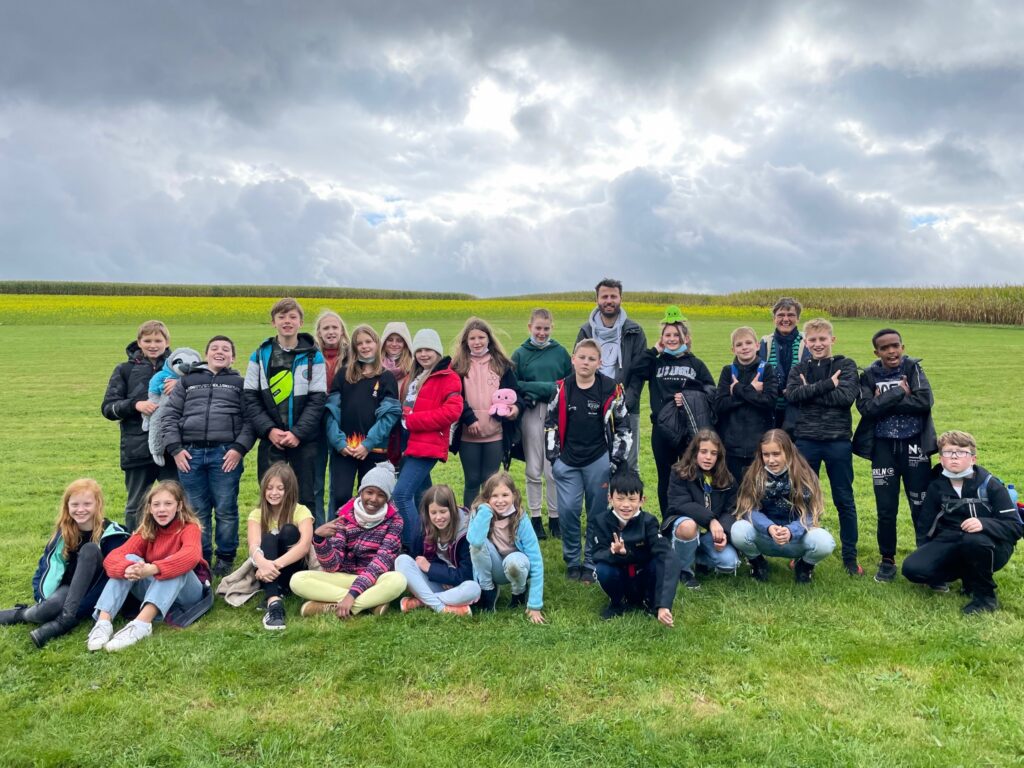 Gruppenfoto von Schülern outdoor auf einer Wiese mit bewölktem Himmel.