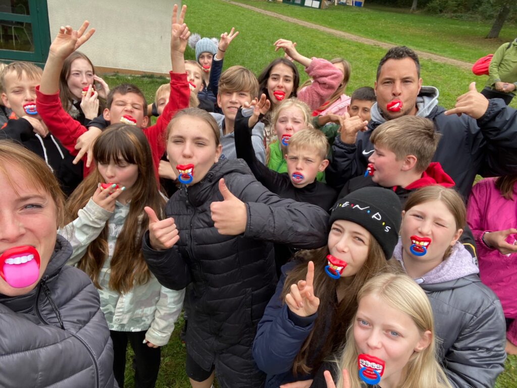 Gruppe von Kindern und Erwachsenen mit bunten Lippen-Fingermasken im Freien.