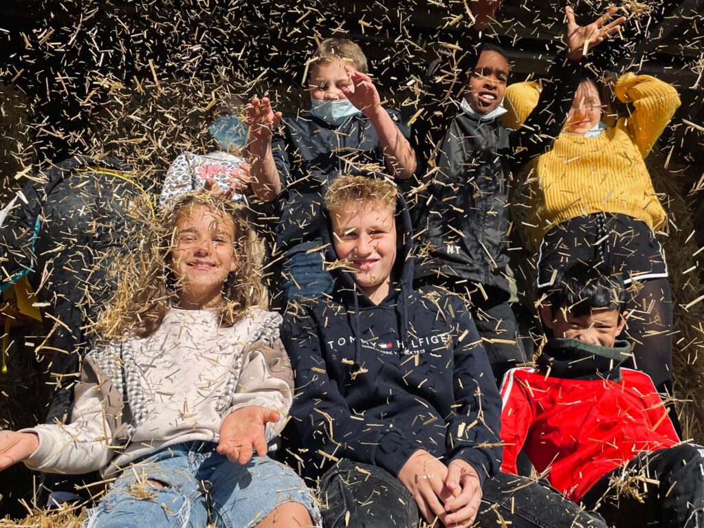 Gruppe von Kindern, die in Heu spielen und lachen.