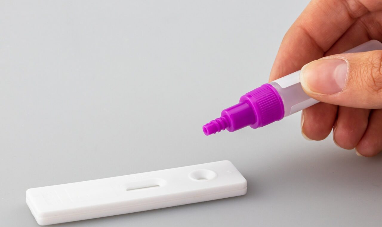 Eine Hand hält einen Markierstift über einem Teststreifen.