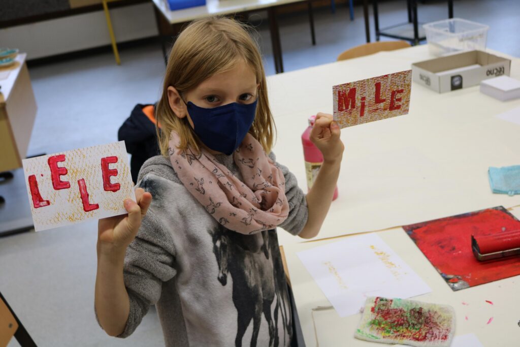 Ein Kind hält zwei Karten mit den Aufschriften "LE" und "MILE" in der Hand.