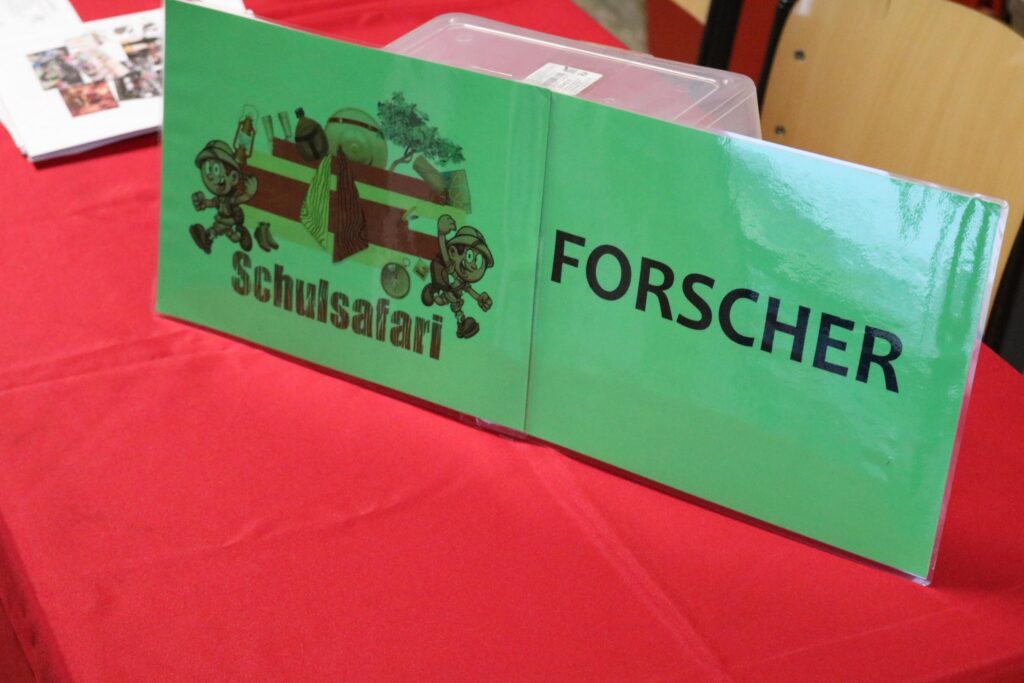 Tisch mit einem grünen Schild "Forscher" und Schul-Safari-Logo.