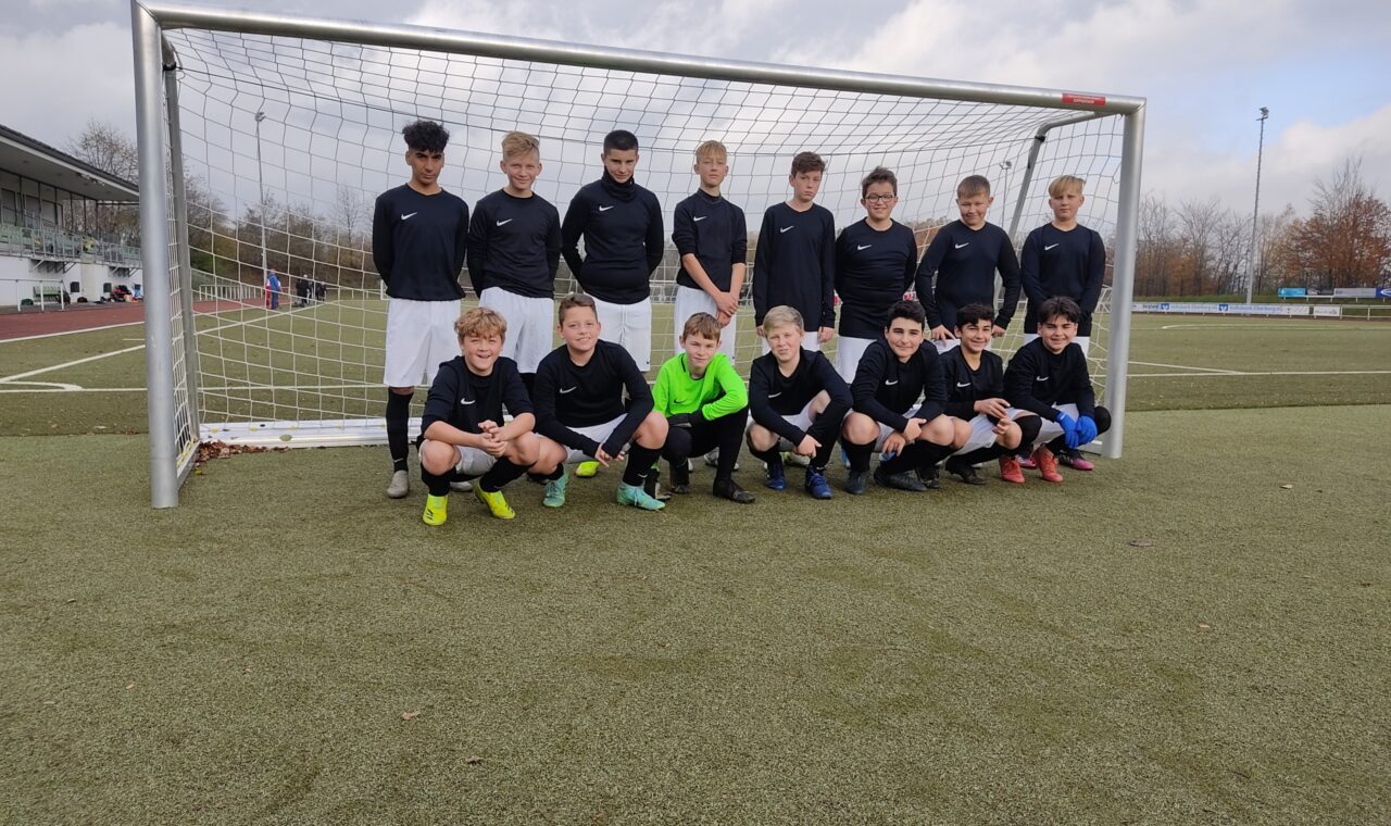 Jugendfußballmannschaft posiert vor dem Tor auf dem Spielfeld.